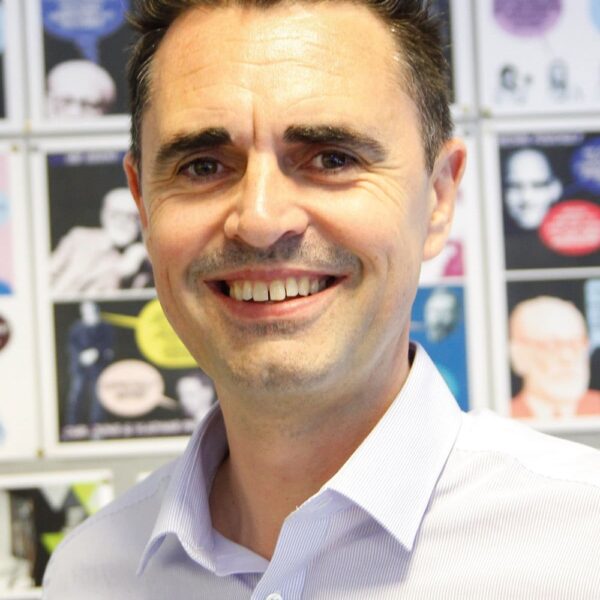 A photo of Lee Clark, Lee is in a shirt and is stood in front of posters.