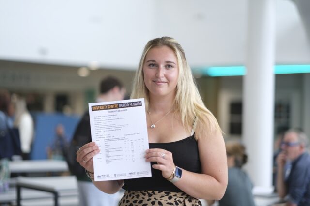 A photo of Lucy, she is wearing a black top and is holding her results up in front of her.