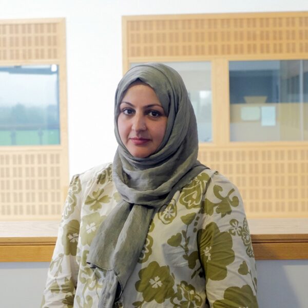 A photo of Sarah, she is wearing a green and cream top with flowers and a green hijab.