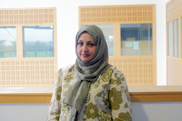 A photo of Sarah, she is wearing a green and cream top with flowers and a green hijab.