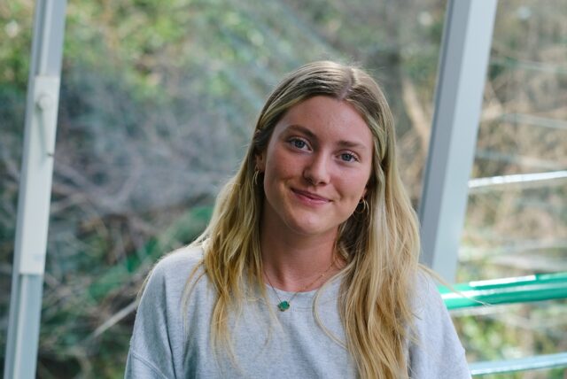 A photo of Sennen, she is wearing a grey sweatshirt and has blonde hair. She smiles at the camera.