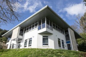 A photo of the Ginkgo building at Tregye. There is grass in the foreground, bare trees to the sides and a large white building in the centre.