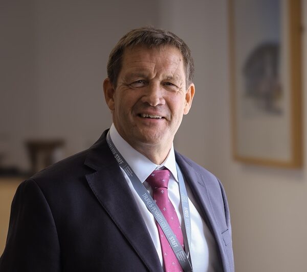 A photo of Martin Tucker. He is wearing a dark suit with a white shirt and pink tie.