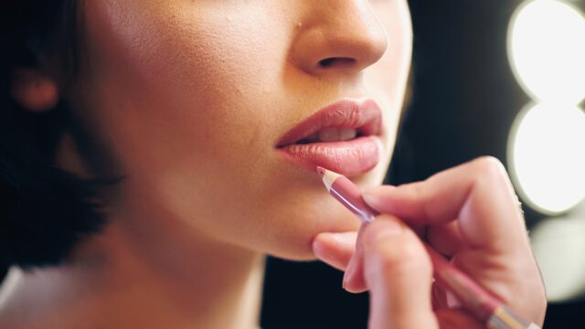 cropped view of makeup artist applying lip pencil on lips of young woman