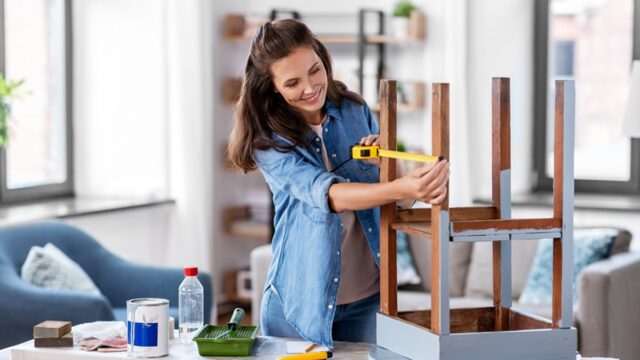 happy smiling woman with ruler measuring old wooden table for renovation