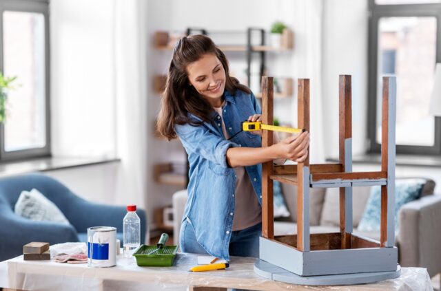 happy smiling woman with ruler measuring old wooden table for renovation