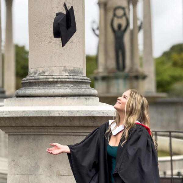 A photo of Emily, she is wearing a graduation gown and she is throwing her cap up in the air.