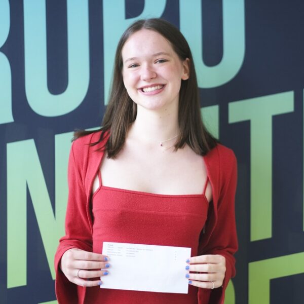 A photo of Mimi, she is wearing a red top and red cardigan and is standing in front of a Truro and Penwith College backdrop.
