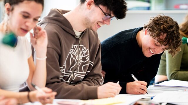 Students sit at a lab table filling out coursework, smiling.