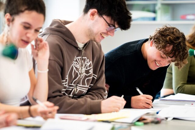 Students sit at a lab table filling out coursework, smiling.