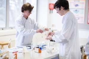 A picture of two students in a laboratory dressed in lab coats doing experiments.