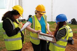 An image of three students in high-vis jackets and hard hats, taking samples and writing out paperwork.