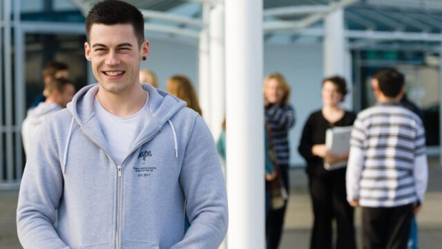 An image of a student stood outside the Fal building smiling at the camera with his hands in his pockets.