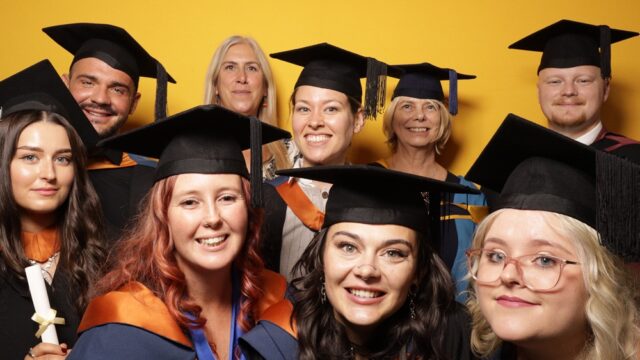 A photo of a group of students smiling at the camera with a yellow backdrop behind them.