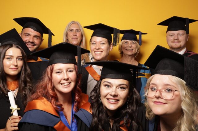A photo of a group of students smiling at the camera with a yellow backdrop behind them.