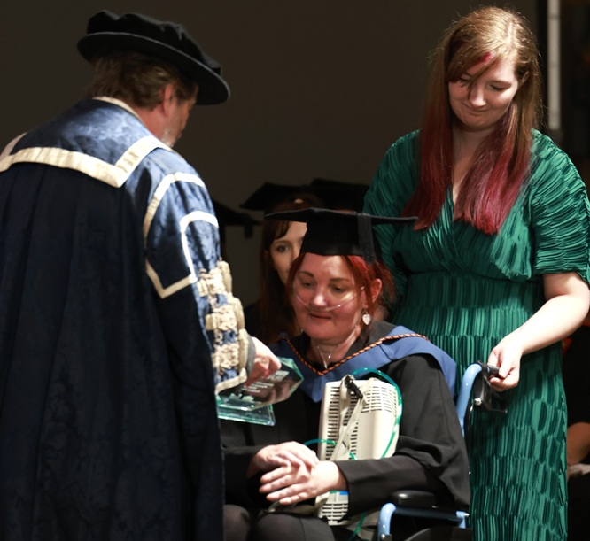 A photo of Rebecca Harvey receiving her award. She is sat in a wheelchair and has an oxygen tank on her lap.