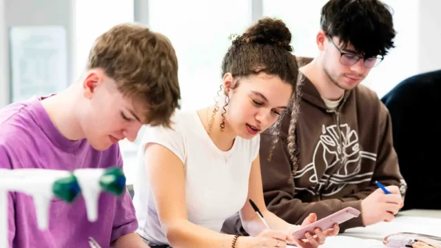 Students sit at lab tables and make notes. One student holds a calculator.