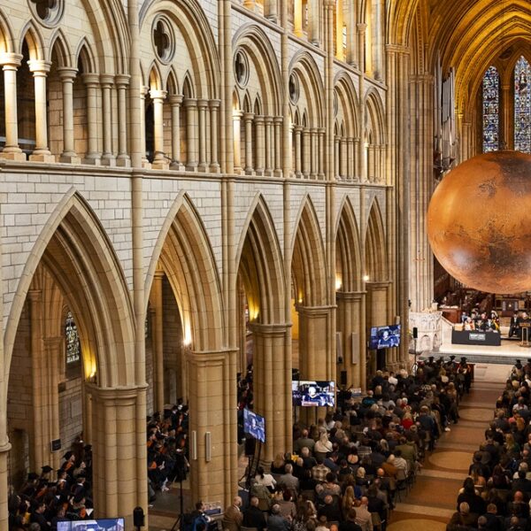 An aerial shot of Truro Cathedral during the University Centre graduation ceremony. People sat in seats and a large replica of Mars hangs over the stage.