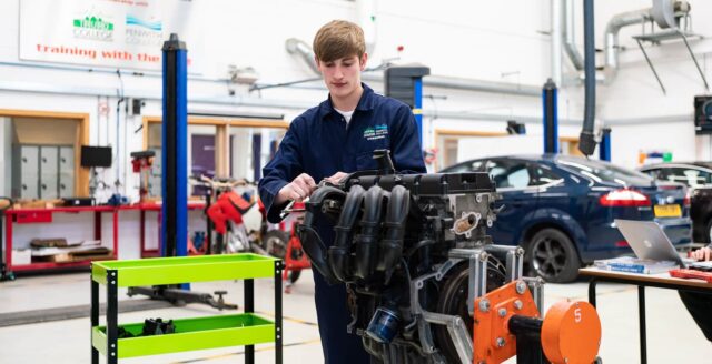 A picture of a student in overalls working on an engine.