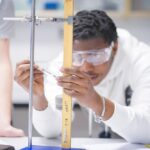 A student in a white jumper and wearing goggles holds a protrator against a long piece of wood.