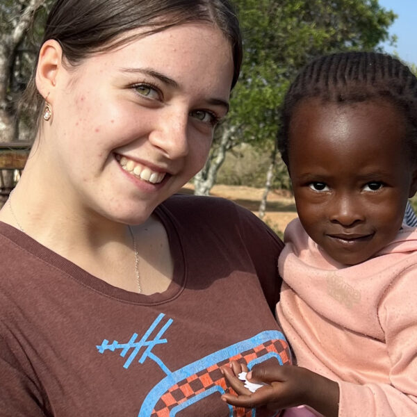 A student smiling at the camera holding a young Eswatini girl in her arms.