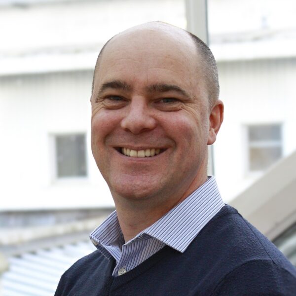 A photo of Matt wearing a jumper and shirt and smiling at the camera.