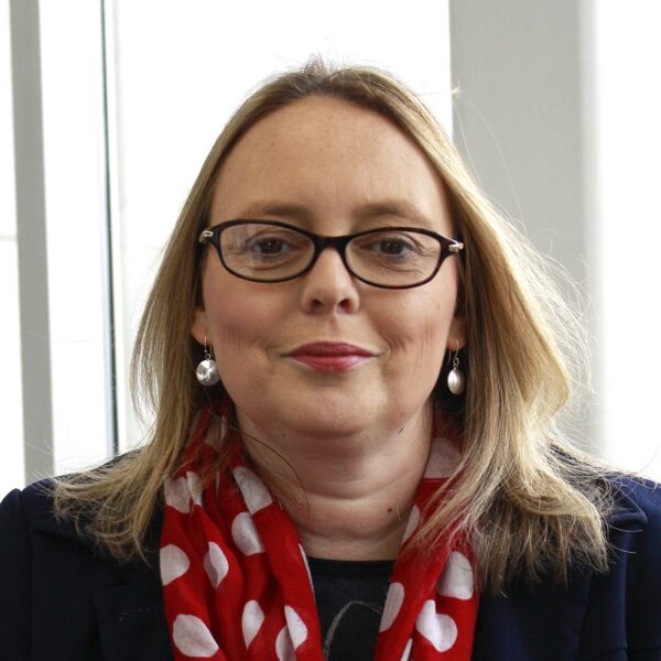 A photo of Nanette wearing a blue blazer and a red scarf.