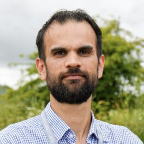 A photo of Tom wearing a check shirt looking at the camera smiling.