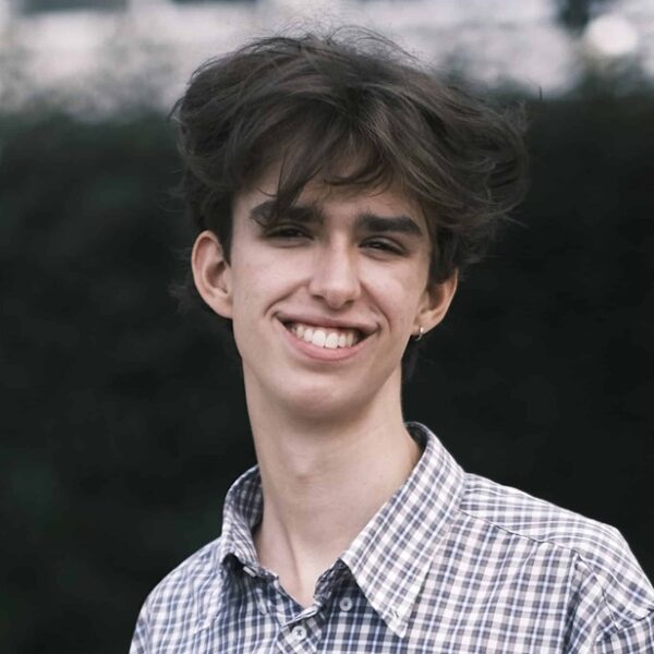 A portrait image of Gabe holding his results. He is outside and wearing a check shirt.