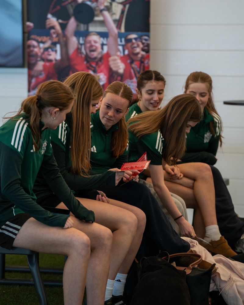 A photo of girls sat on a bench in football kit.