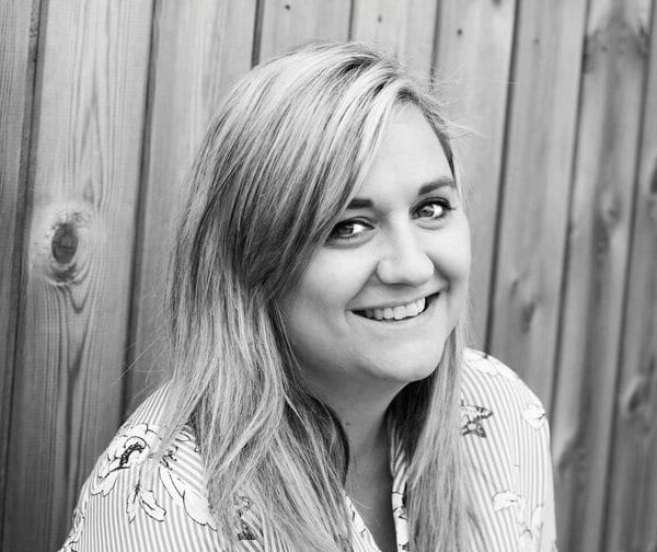 A black and white photo of a woman who is smiling at the camera and wearing a striped shirt.