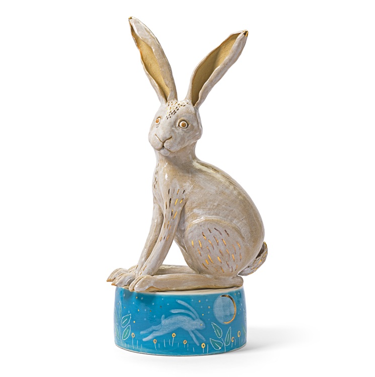 A rabbit sculpture sat on a blue box. Gold markings on the rabbit.