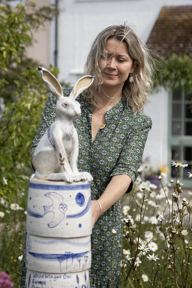 A woman stands in a garden in front of a pottery sculpture. The sculpture is of a rabbit.