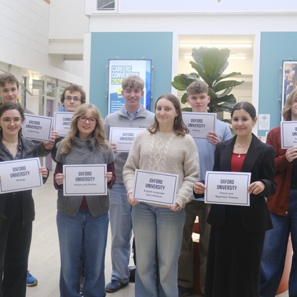A group of students hold up signs which say which university they are going to and what they are studying.
