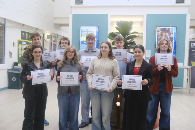A group of students hold up signs which say which university they are going to and what they are studying.