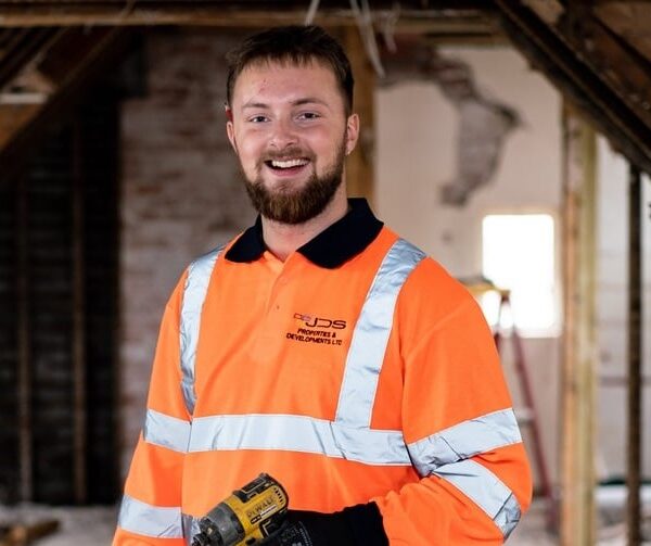 A construction apprentice holding an electric drill in the loft of a newly constructed building.