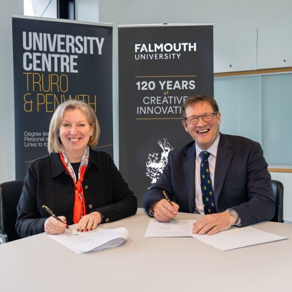 Martin Tucker and Emma Hunt sign paperwork sat at a table with Truro and Penwith and Falmouth University pull ups behind them.