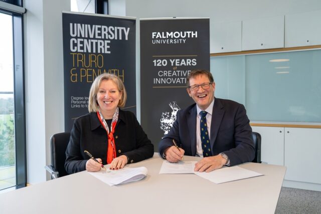 Martin Tucker and Emma Hunt sign paperwork sat at a table with Truro and Penwith and Falmouth University pull ups behind them.