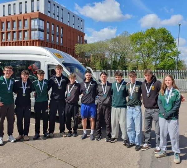 A group of students stood outside with their arms around each other and medals around their necks.
