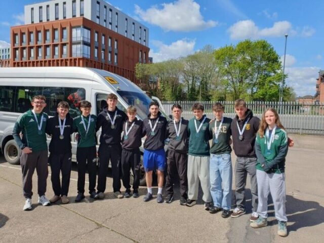 A group of students stood outside with their arms around each other and medals around their necks.