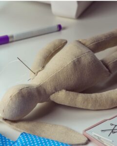 A plain handmade doll with a threading needle through its arm.