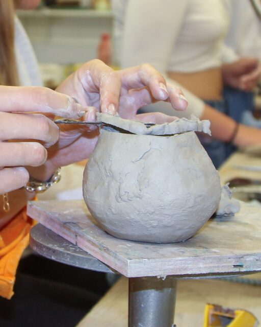 Hands working on a piece of pottery on a potters wheel.