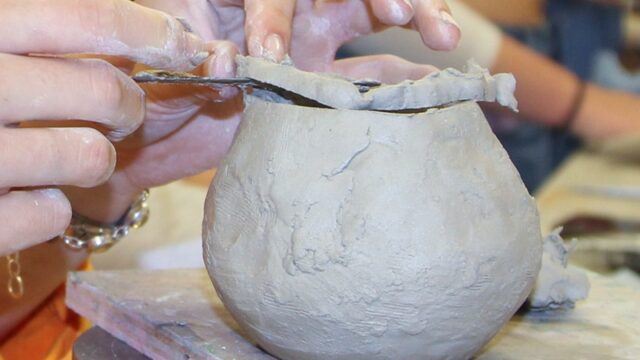 Hands working on a piece of pottery on a potters wheel.