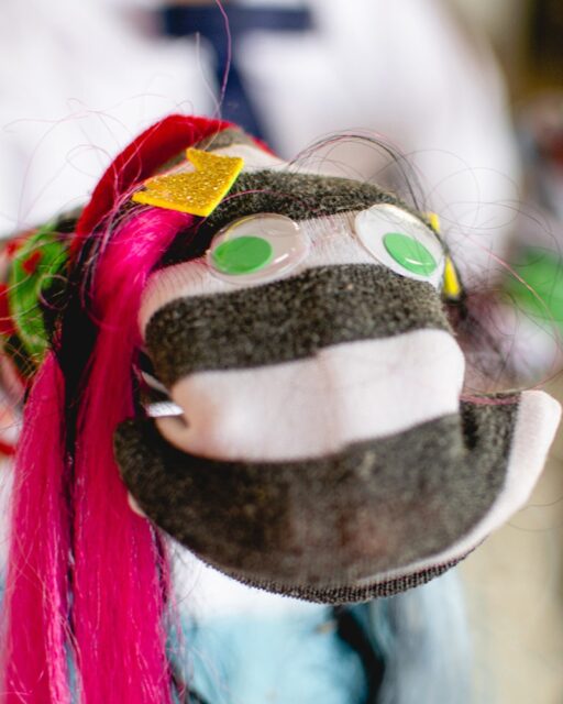 A puppet with googly eyes, a little crown and pink hair.