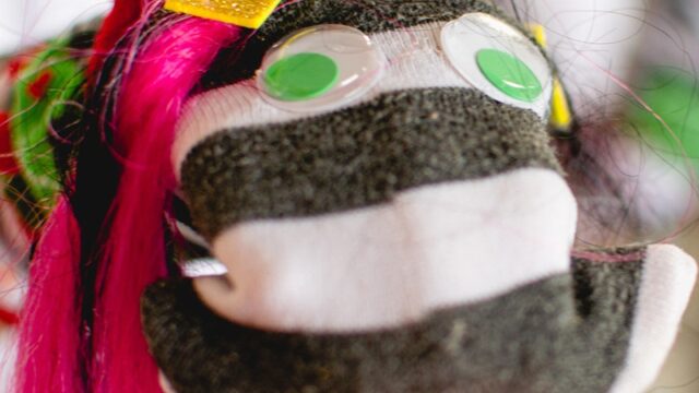 A puppet with googly eyes, a little crown and pink hair.