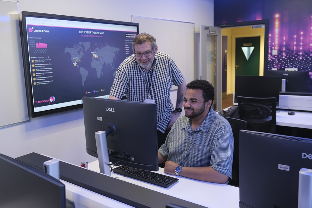 Two people sit at computers in a computer room.