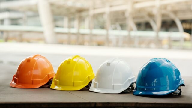A row of four hard hats in orange, yellow, white and blue.