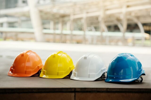 A row of four hard hats in orange, yellow, white and blue.