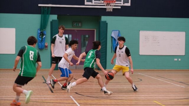 Students playing basketball in a sports hall.