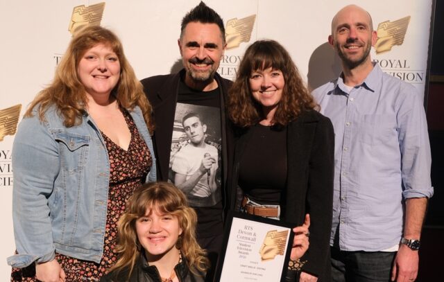 Lecturers and senior management stand with a student who has received an award.